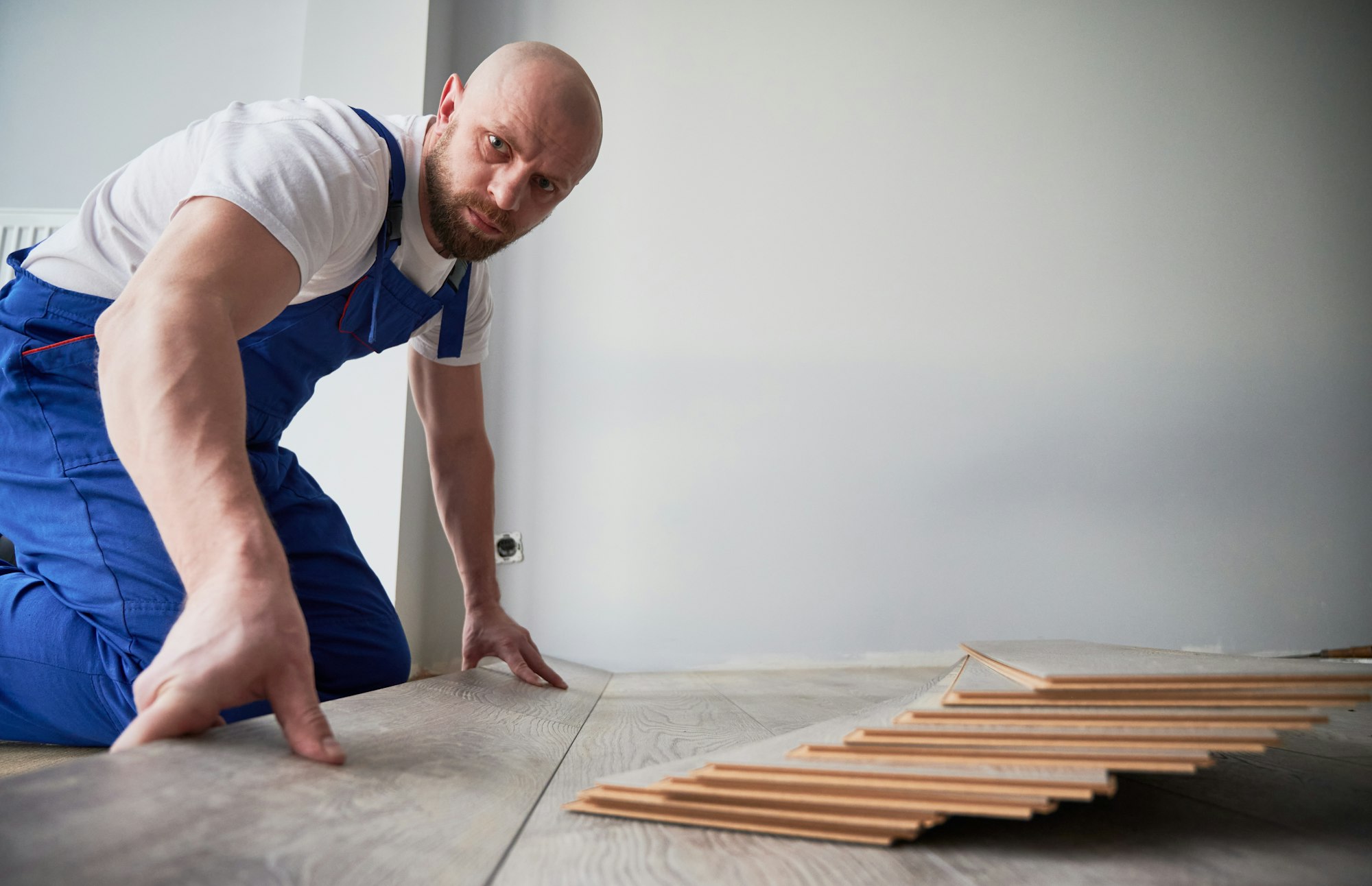 Bearded man installing laminate wood floor in apartment.